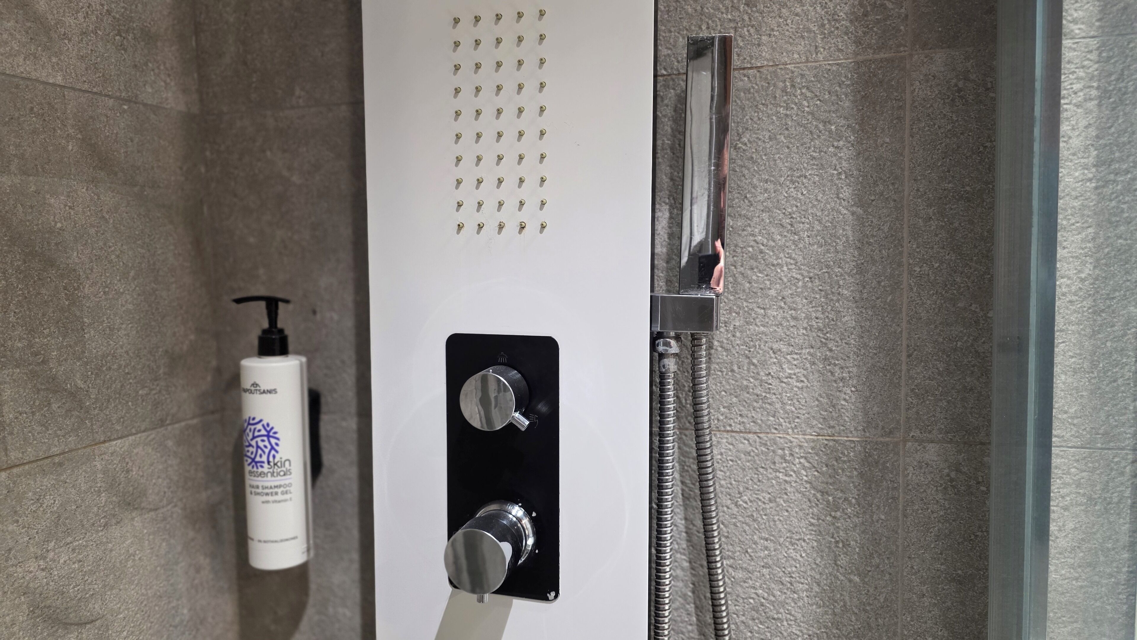 A shower with a control panel, a handheld showerhead, and a bottle of shampoo.