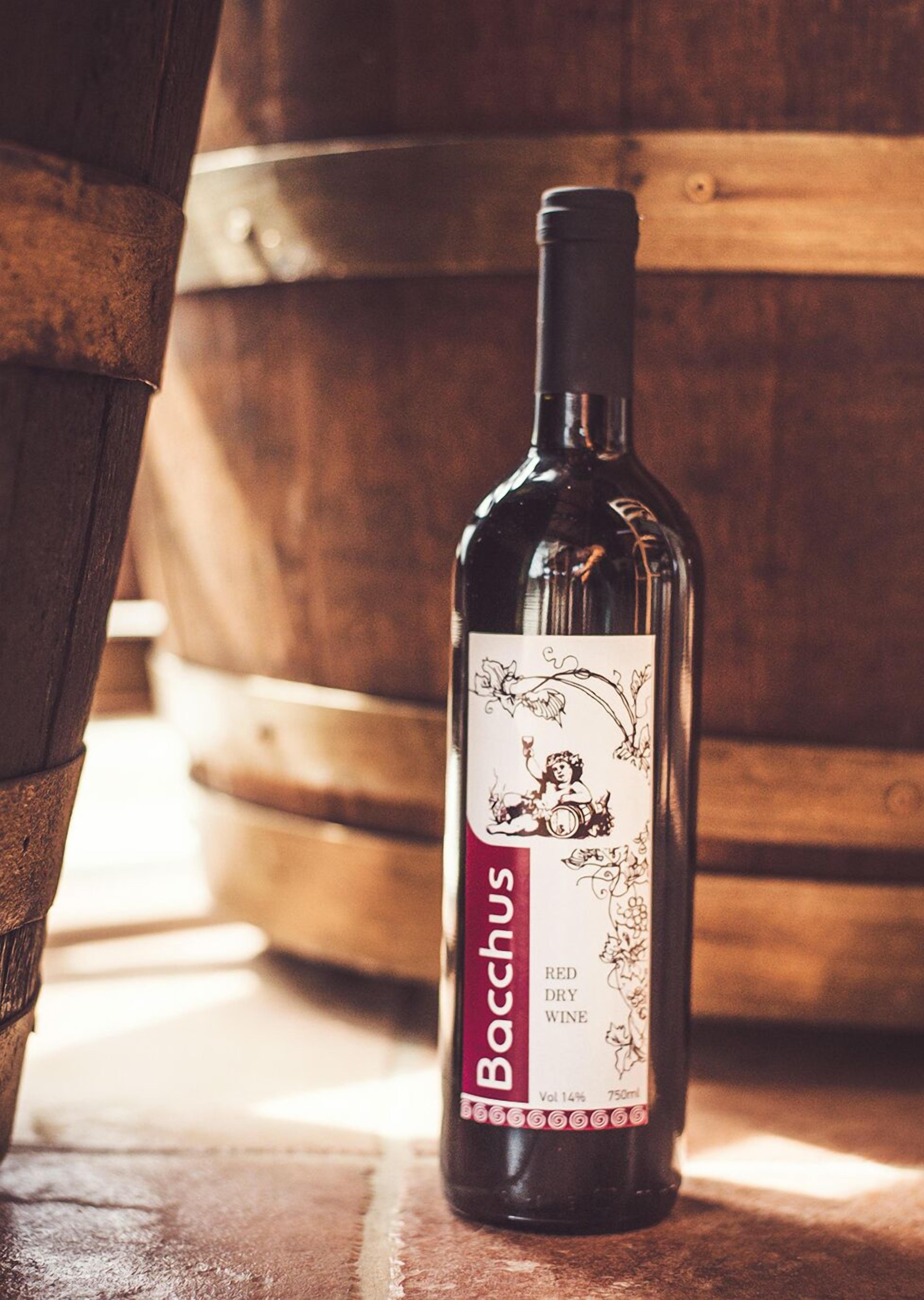 Una botella de vino tinto seco con etiqueta que presenta una ilustración antigua de una mujer y un niño, colocada frente a barriles de madera.