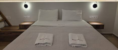 A hotel room with a large bed, two pillows, two bedside lamps, and two folded towels on the bed.
