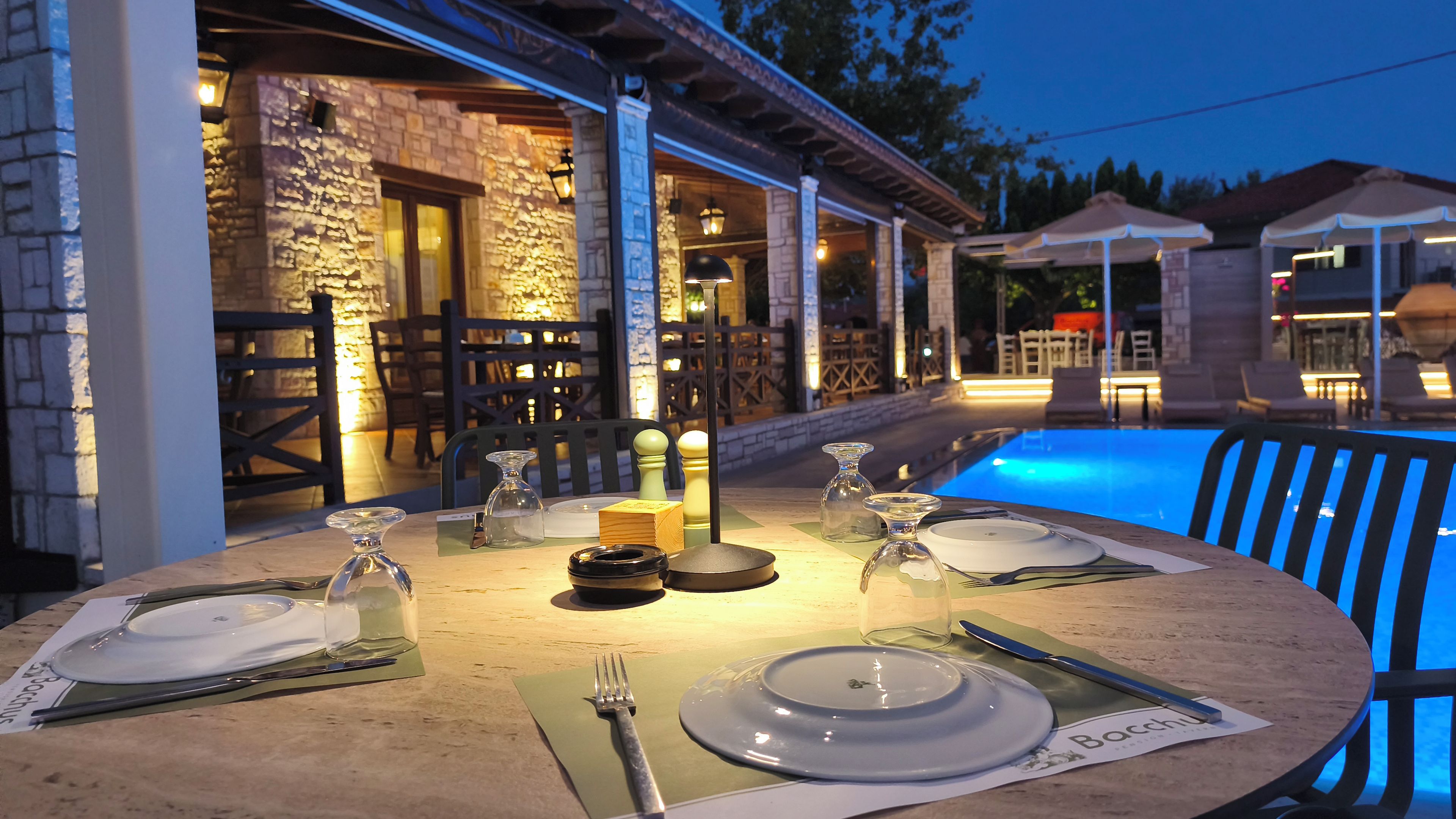 An outdoor dining area with a table set for four, surrounded by stone walls and a pool.