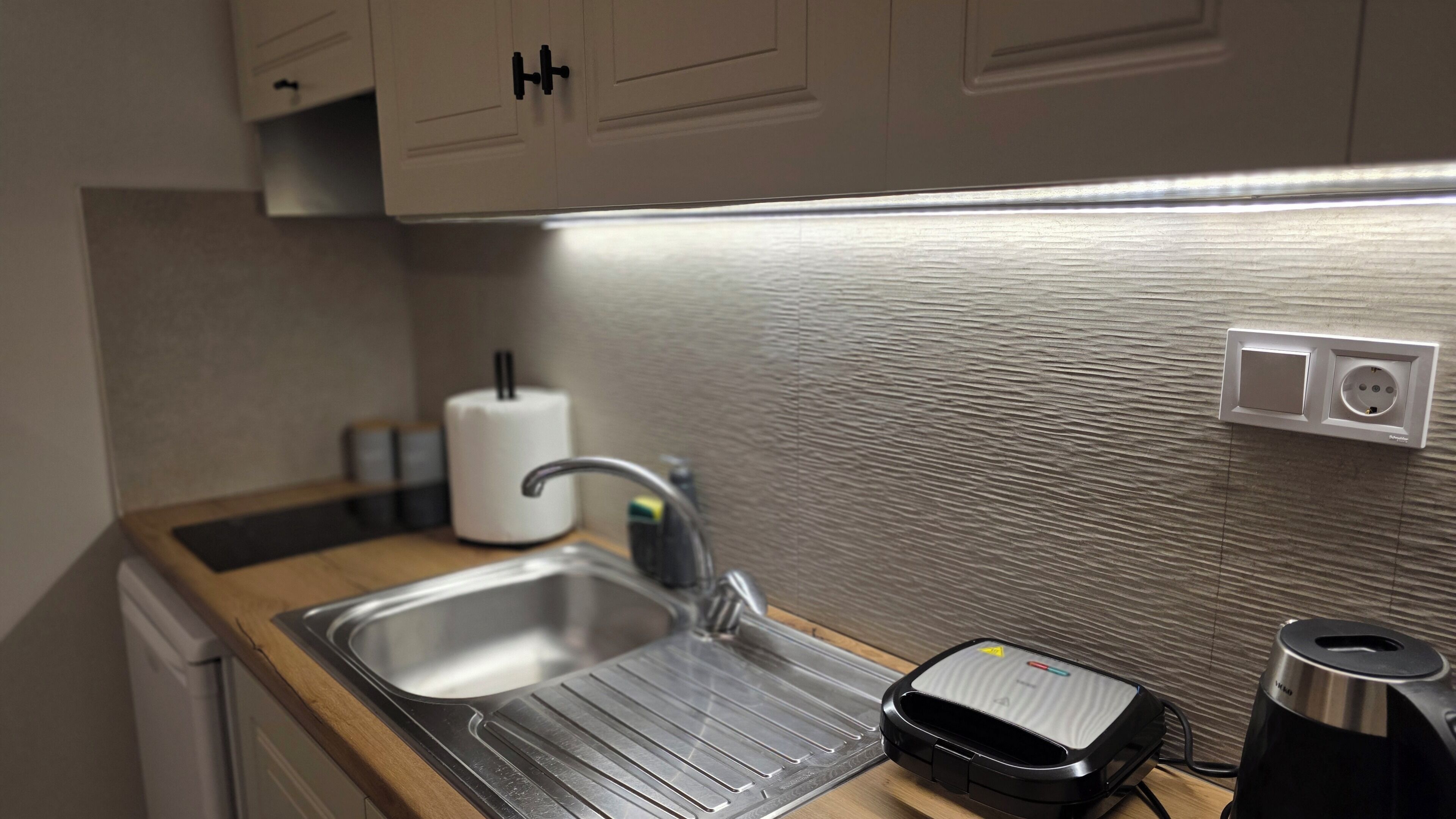Una cocina moderna con un lavamanos de acero inoxidable, una tetera y un tostador.