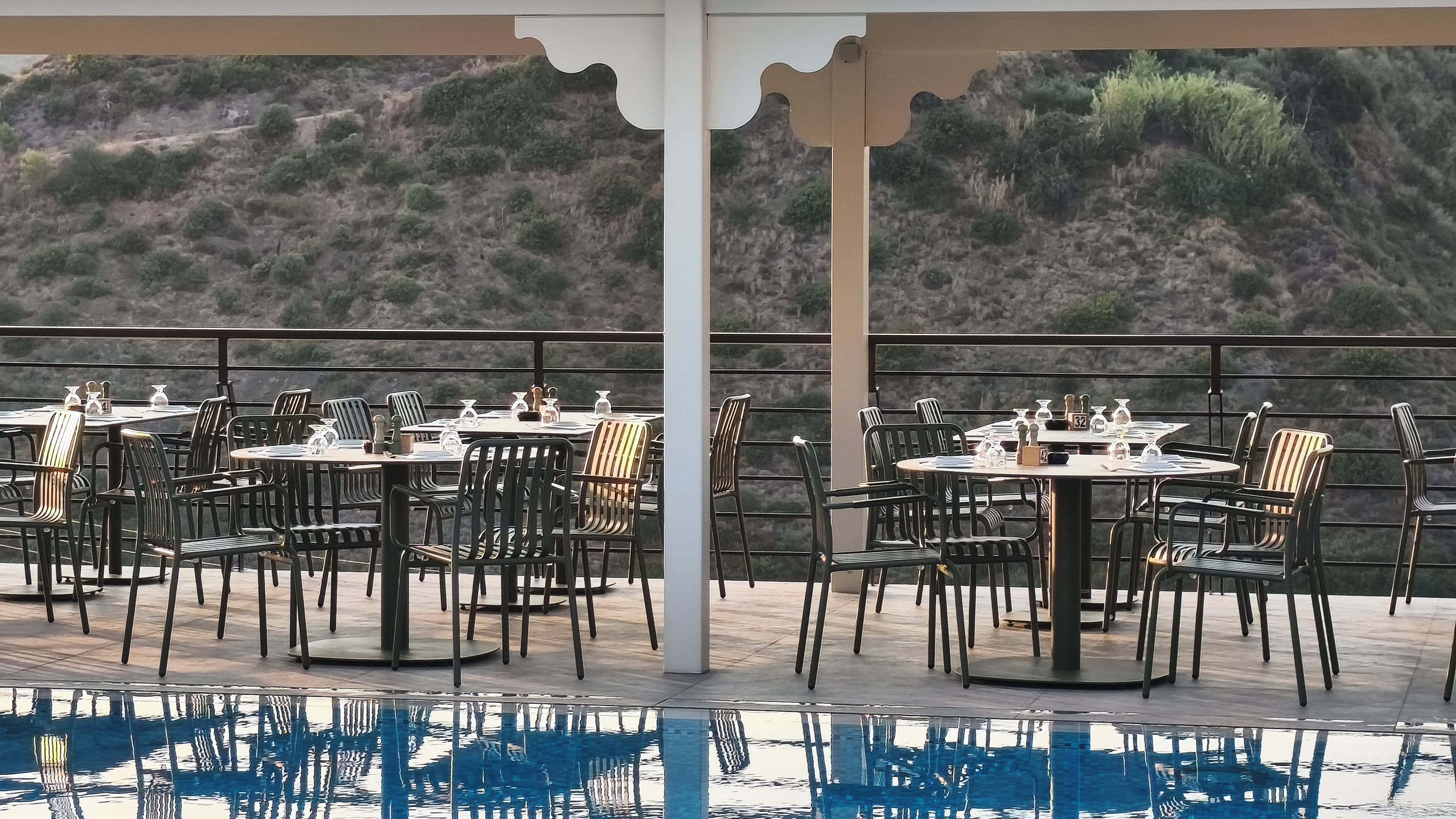 Un espace extérieur aménagé pour les repas, avec des tables et des chaises, une piscine et une vue sur un paysage vallonné.