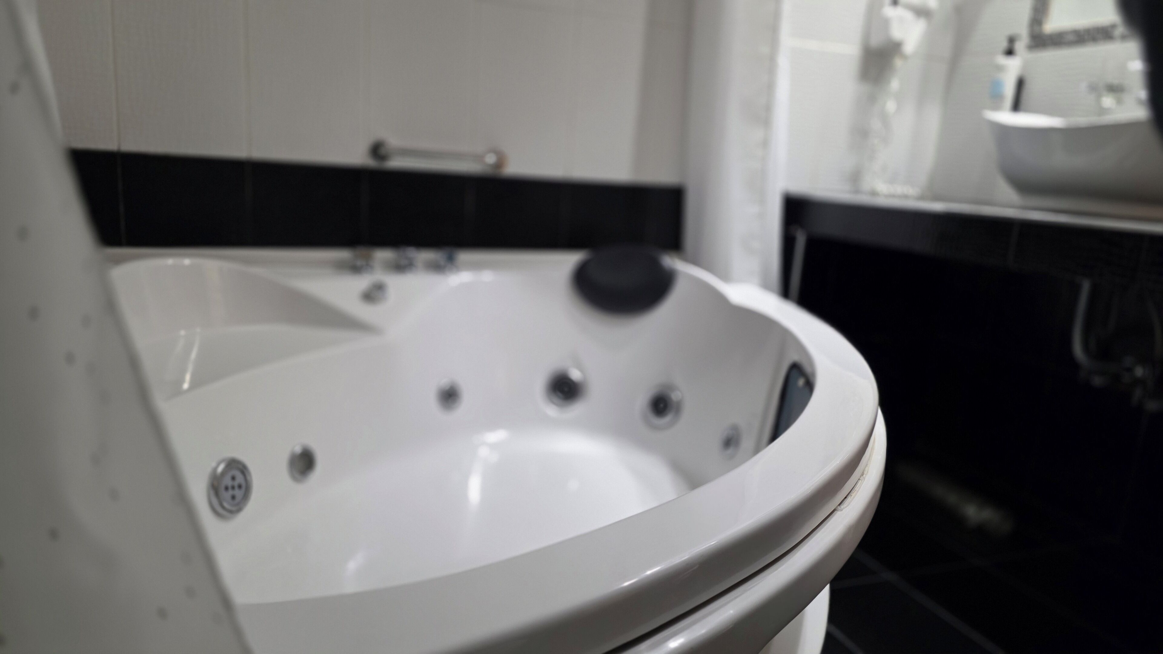 A white bathtub with multiple jets, a control panel, and a black tiled wall in the background.