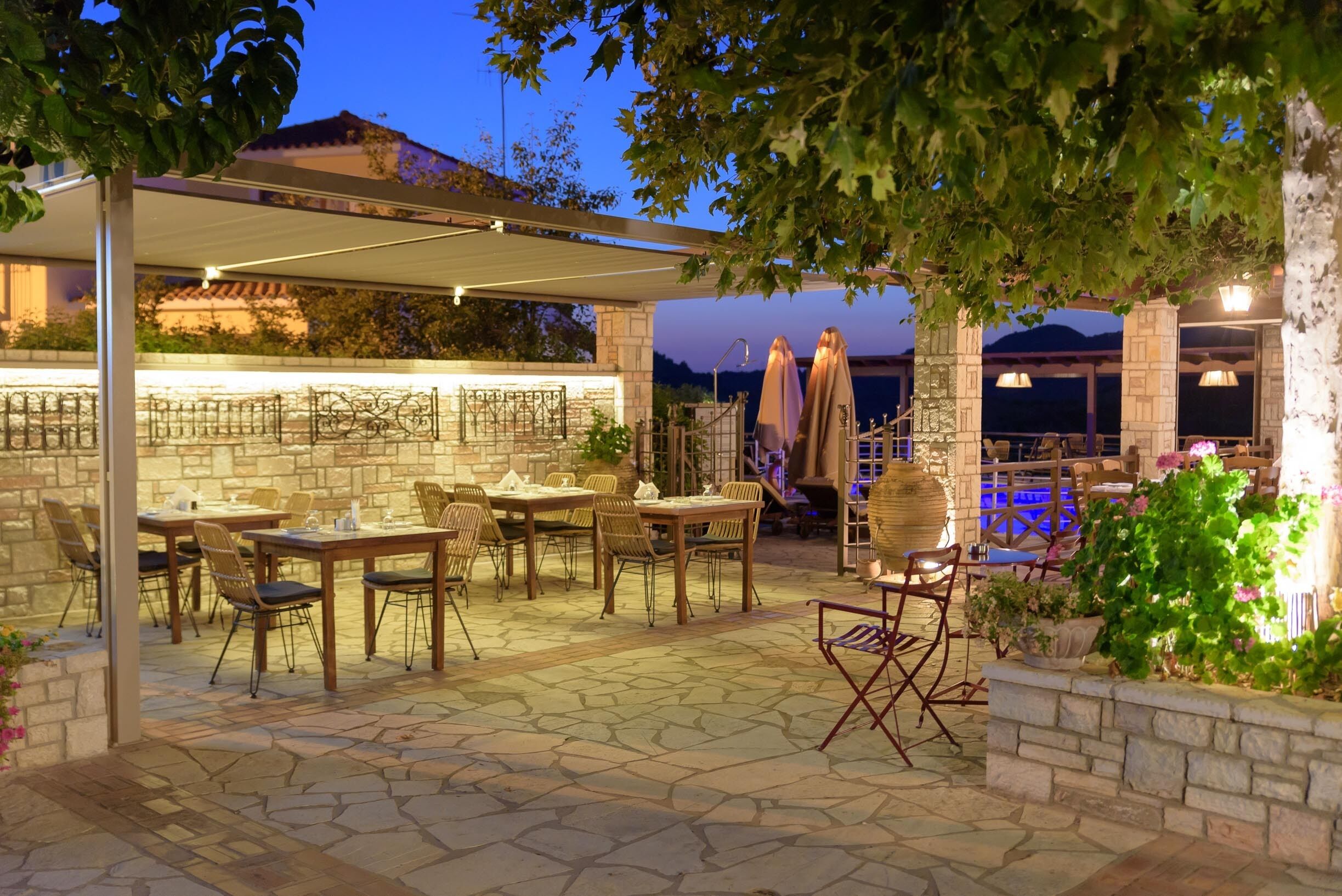 An outdoor patio area with stone flooring, wooden tables and chairs, and a covered seating area.