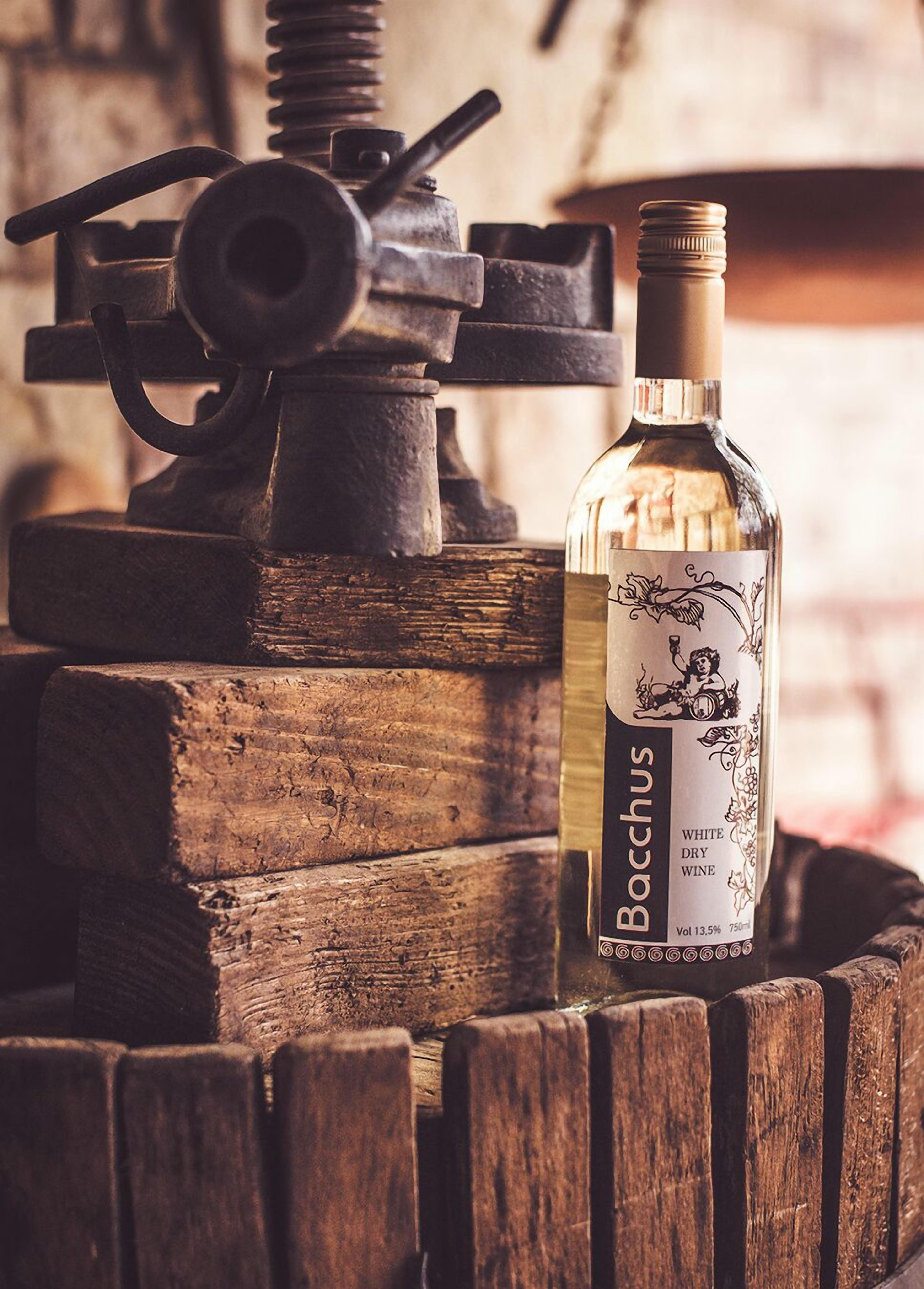 A bottle of Boccus white dry wine placed on a wooden barrel with a vintage press in the background.