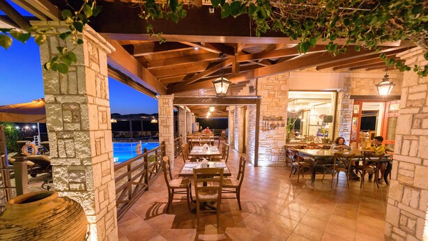 Un área de comedor al aire libre con muros de piedra y vigas de madera, con mesas y sillas dispuestas para los huéspedes.
