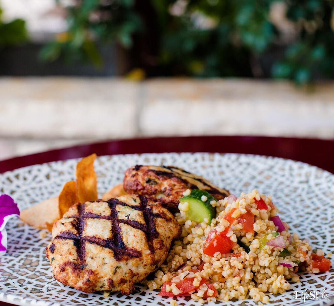 A plate with grilled chicken patties, couscous salad, and a side of fries.