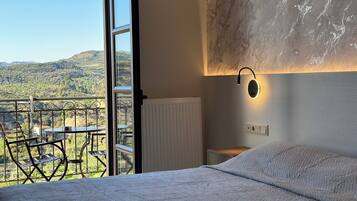 Een slaapkamer met een groot bed, een nachtkastje, een wandlamp en uitzicht op een balkon met een tafel en stoelen.