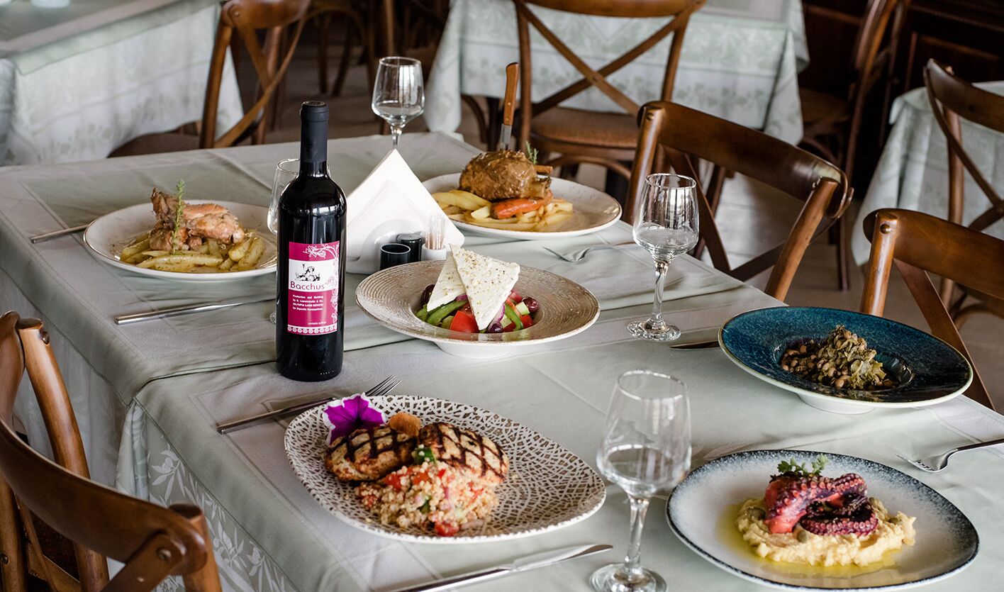A dining table with plates of food, wine glasses, and a bottle of wine.