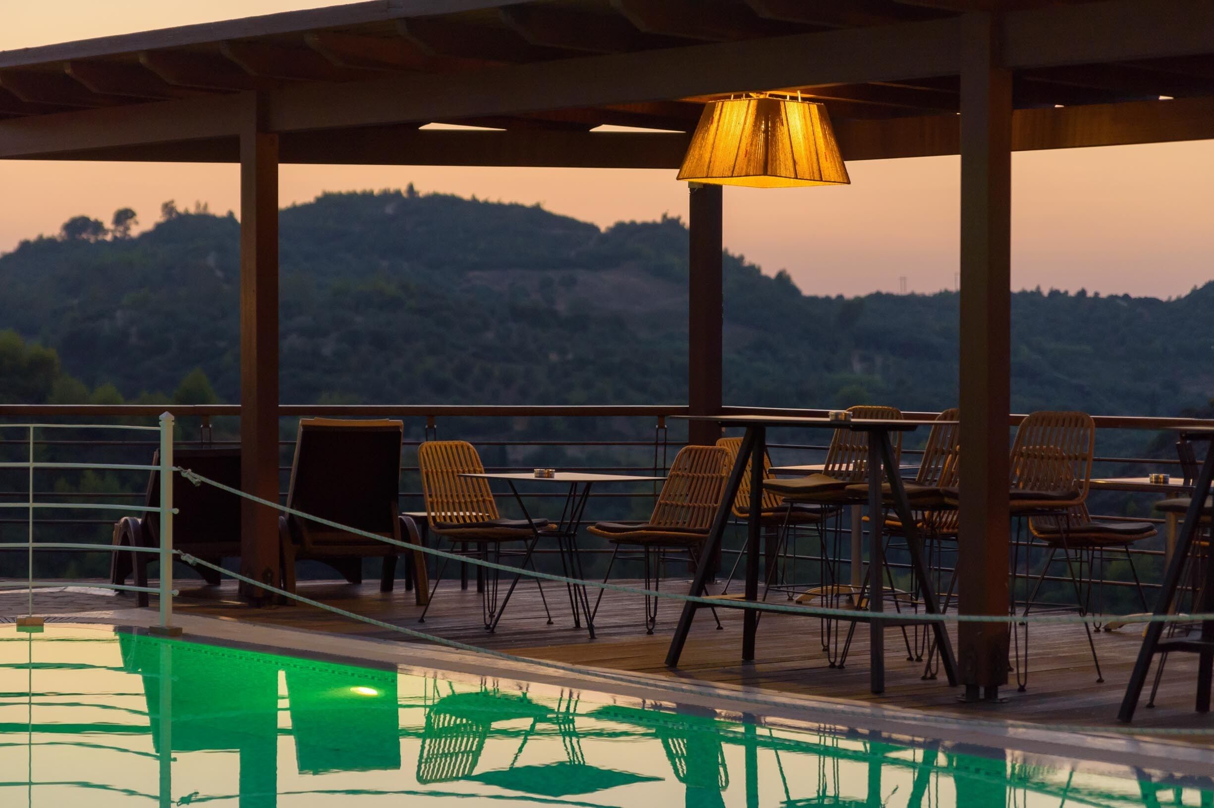 Un área de estar al aire libre con sillas y mesas, con vista a una piscina y un paisaje montañoso.