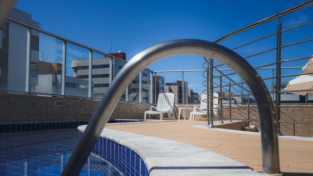 A rooftop pool area with a clear blue sky, a metal pool ladder, and white lounge chairs.