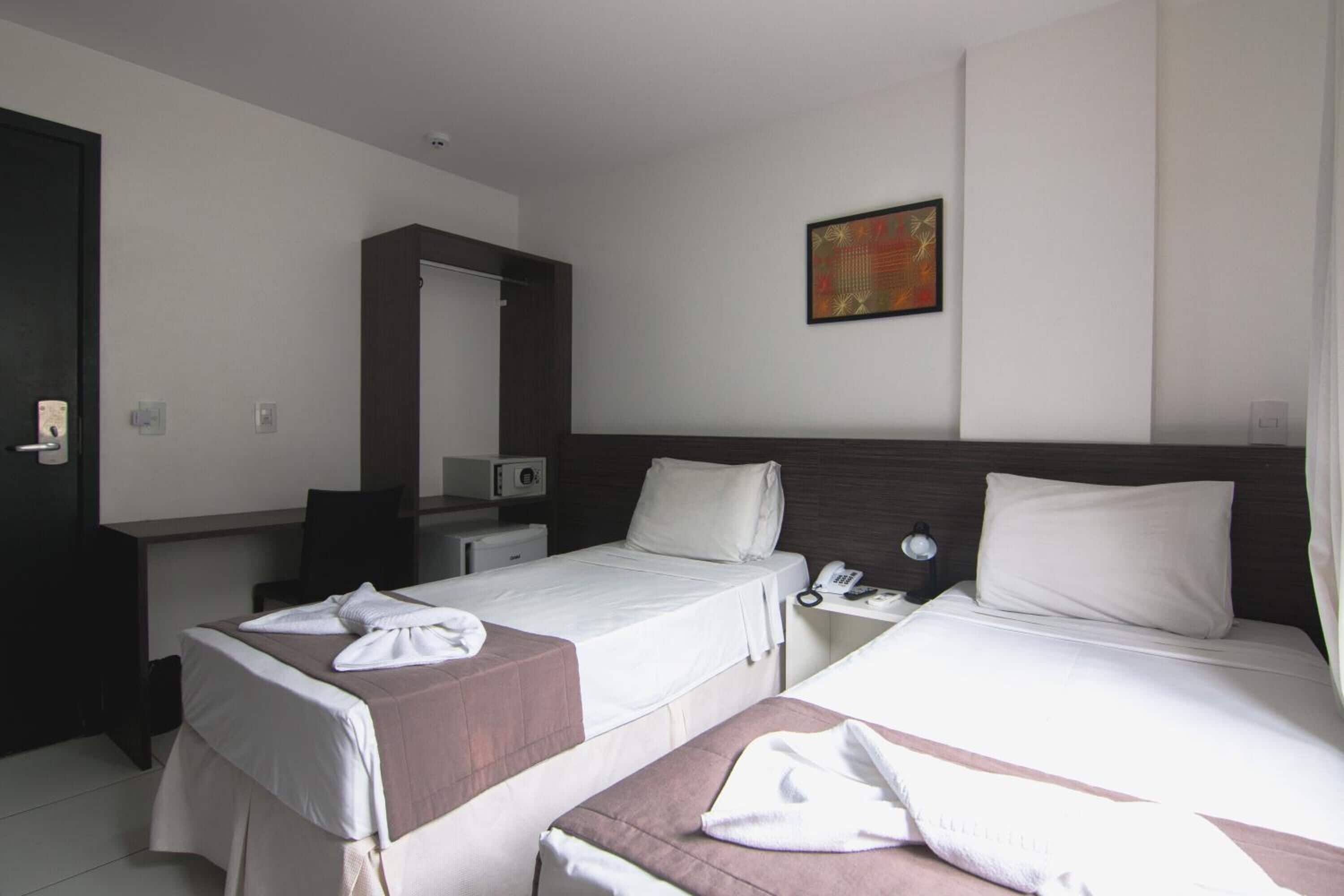 A hotel room with two beds, a desk, a chair, a mirror, and a painting on the wall.