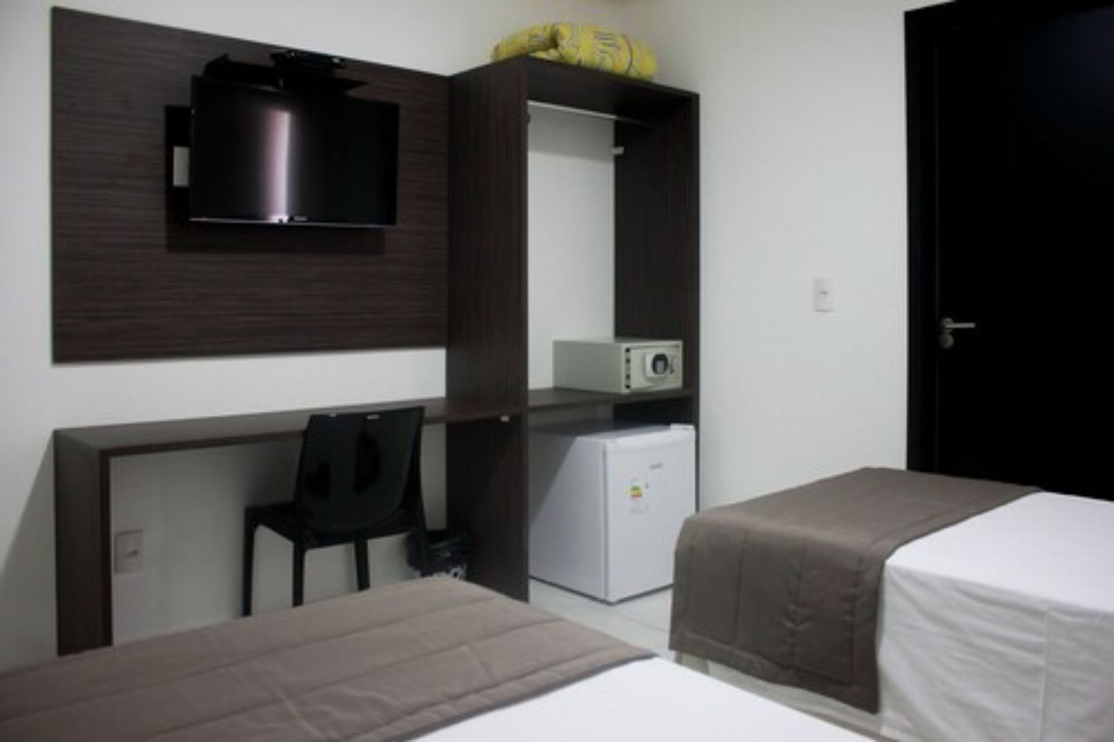 A compact hotel room with a bed, a desk with a chair, a small refrigerator, and a microwave.