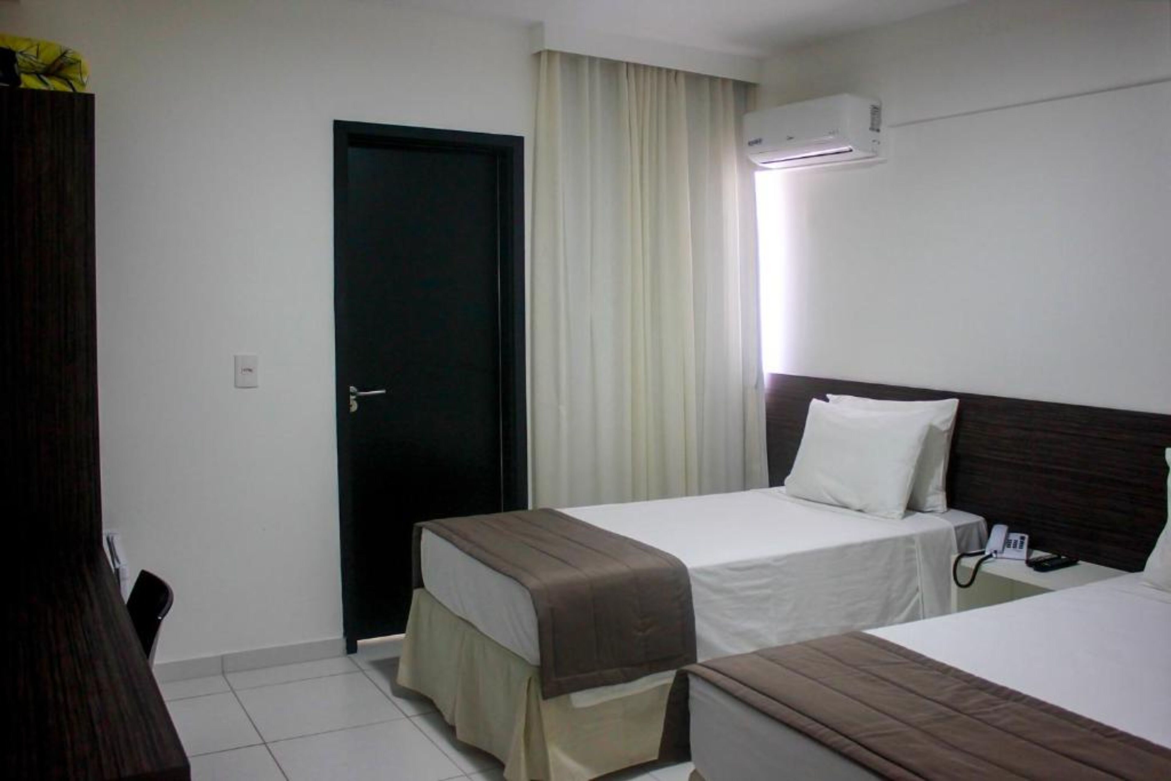 A hotel room with two beds, a door, an air conditioning unit, and a telephone on the nightstand.