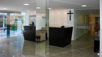 Una moderna área de recepción con un panel de vidrio, un mostrador de recepción y una cruz en la pared.