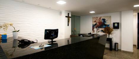 A modern reception desk with a black marble top, a Samsung monitor, and a cross on the wall.