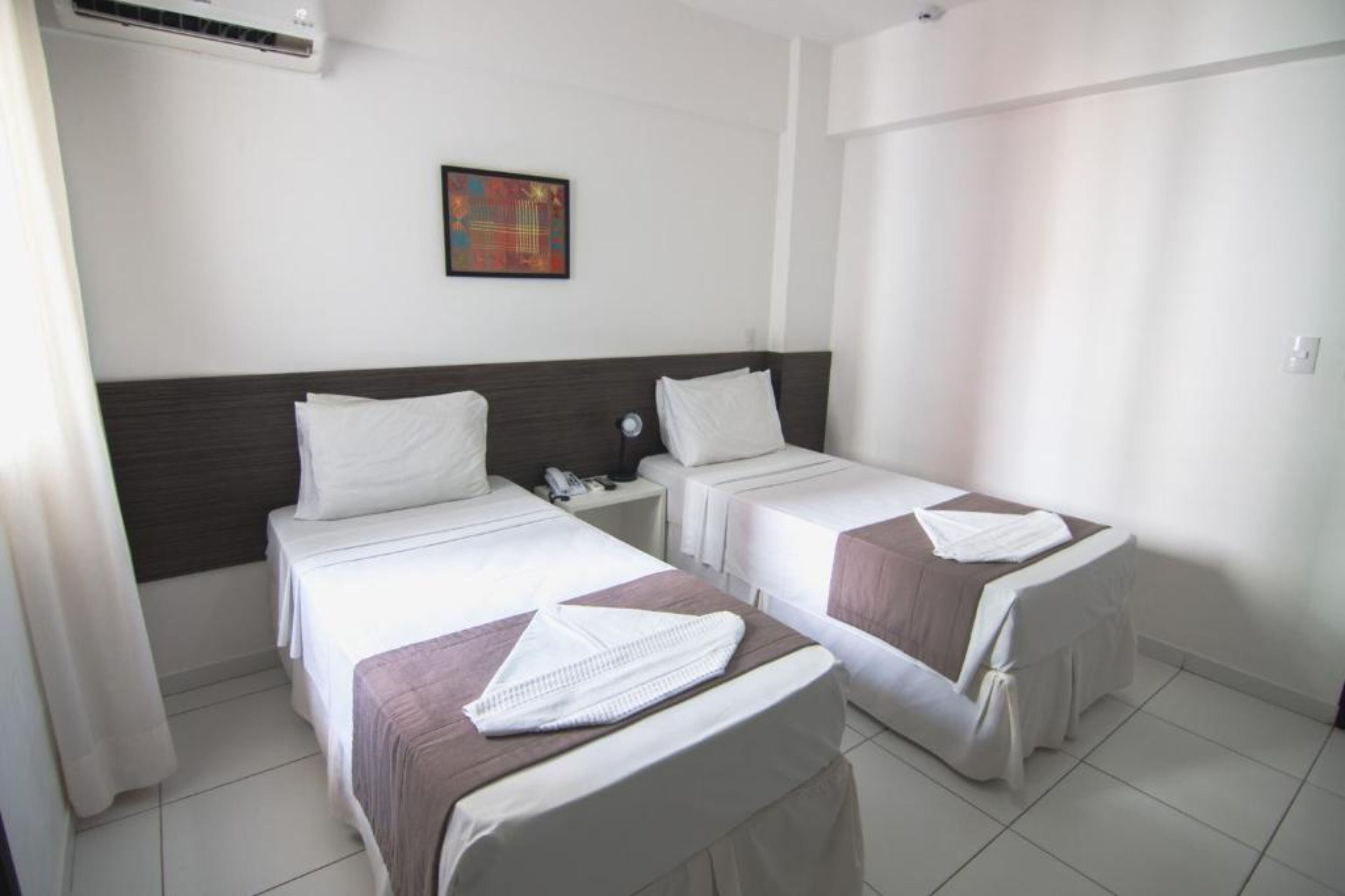 Una habitación de hotel con dos camas, una mesita de noche, aire acondicionado en la pared y un cuadro.