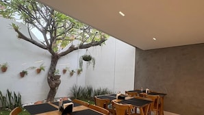 A modern dining area with wooden tables and chairs, a large tree, and potted plants.
