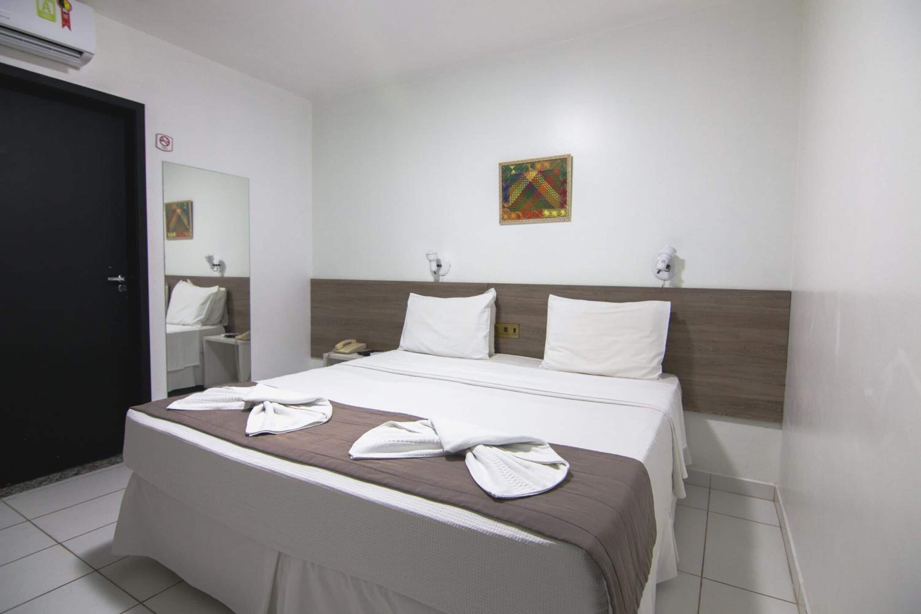 Une chambre d’hôtel comprenant un lit, une table de chevet, un miroir, une œuvre d’art accrochée au mur et une porte.