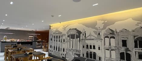 Un restaurante con mesas y sillas, un mural en la pared y una barra con productos alimenticios.