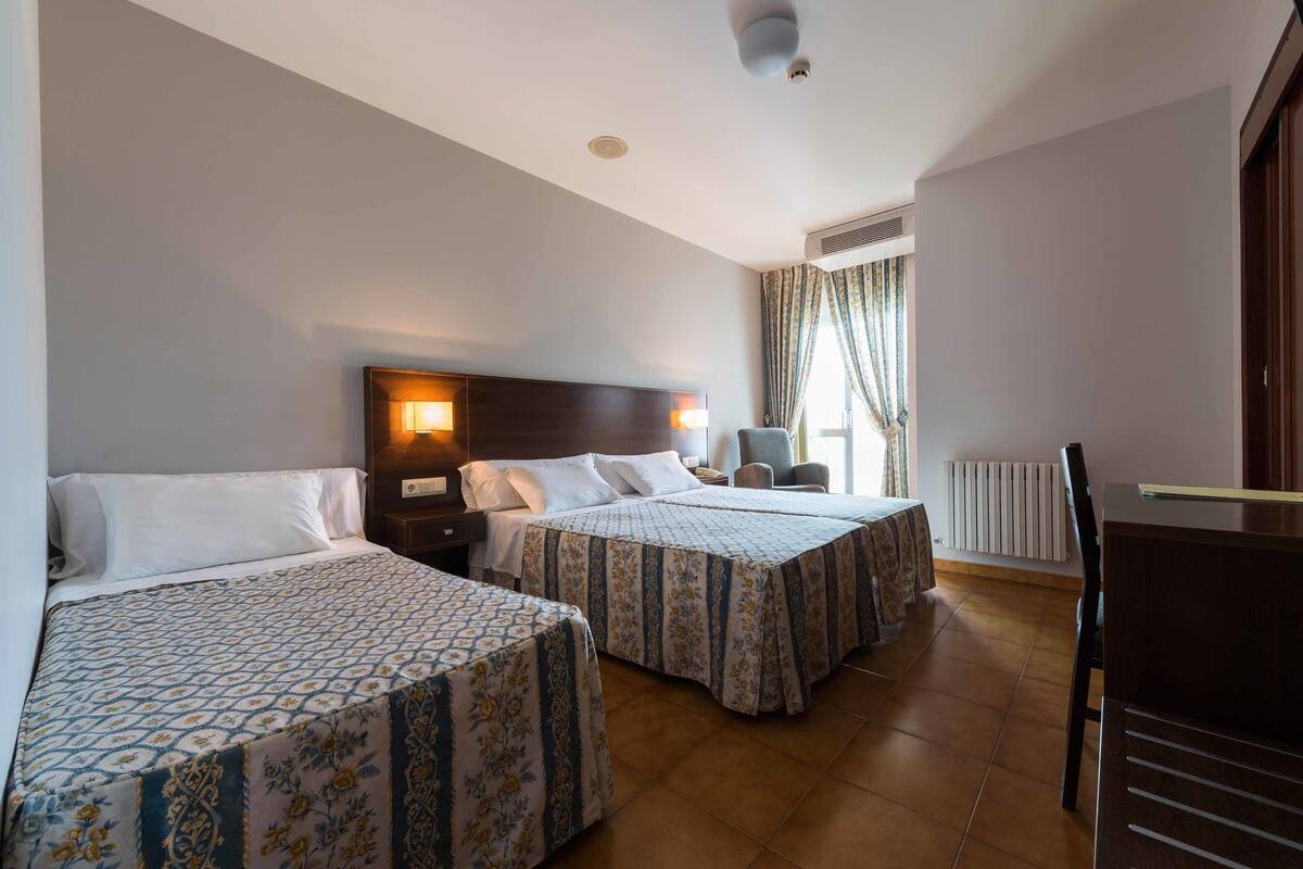 A hotel room with two beds, a desk, a chair, and a window with curtains.