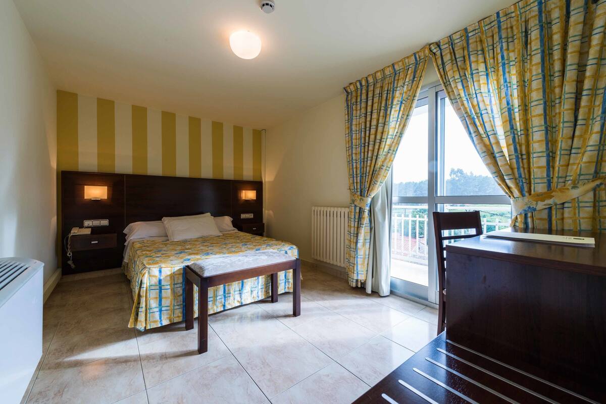 A bedroom with a bed, bedside tables, a desk, and a window with curtains.