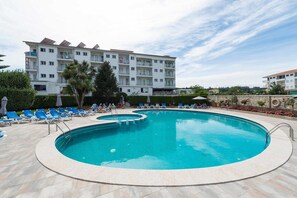 A swimming pool with blue water, surrounded by lounge chairs and a building with balconies in the background. - Troncoso (Sanxenxo)