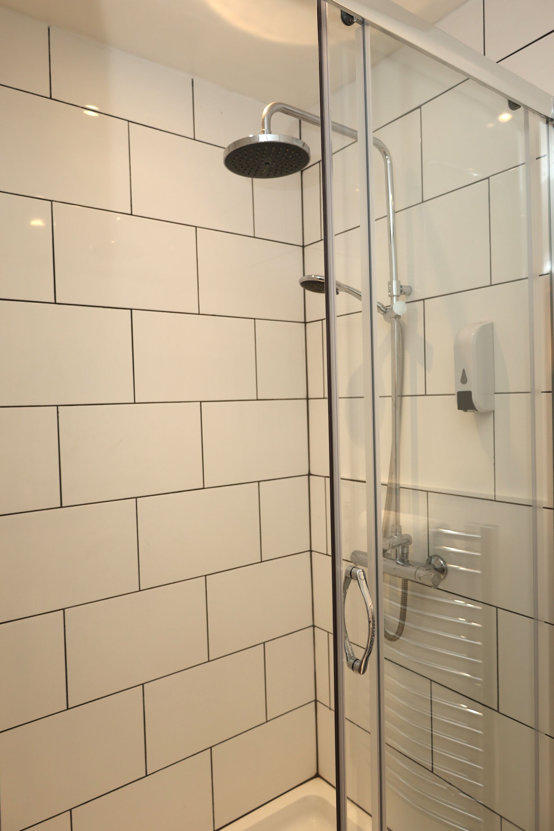 Een douchecabine met glazen wanden, een handdouche en een wandmengkraan.