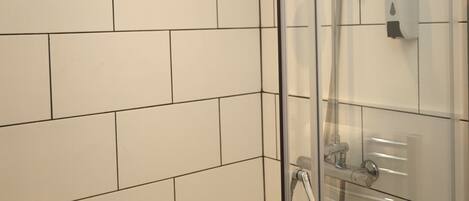 Een douchecabine met glazen wanden, een handdouche en een wandmengkraan.