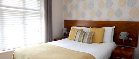 A neatly made bed with a wooden headboard, two bedside lamps, and a patterned wall.