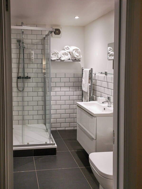 A modern bathroom with a glass-enclosed shower, white tiled walls, a white sink, and a toilet. - The Olde Kings Arms (Hemel Hempstead)