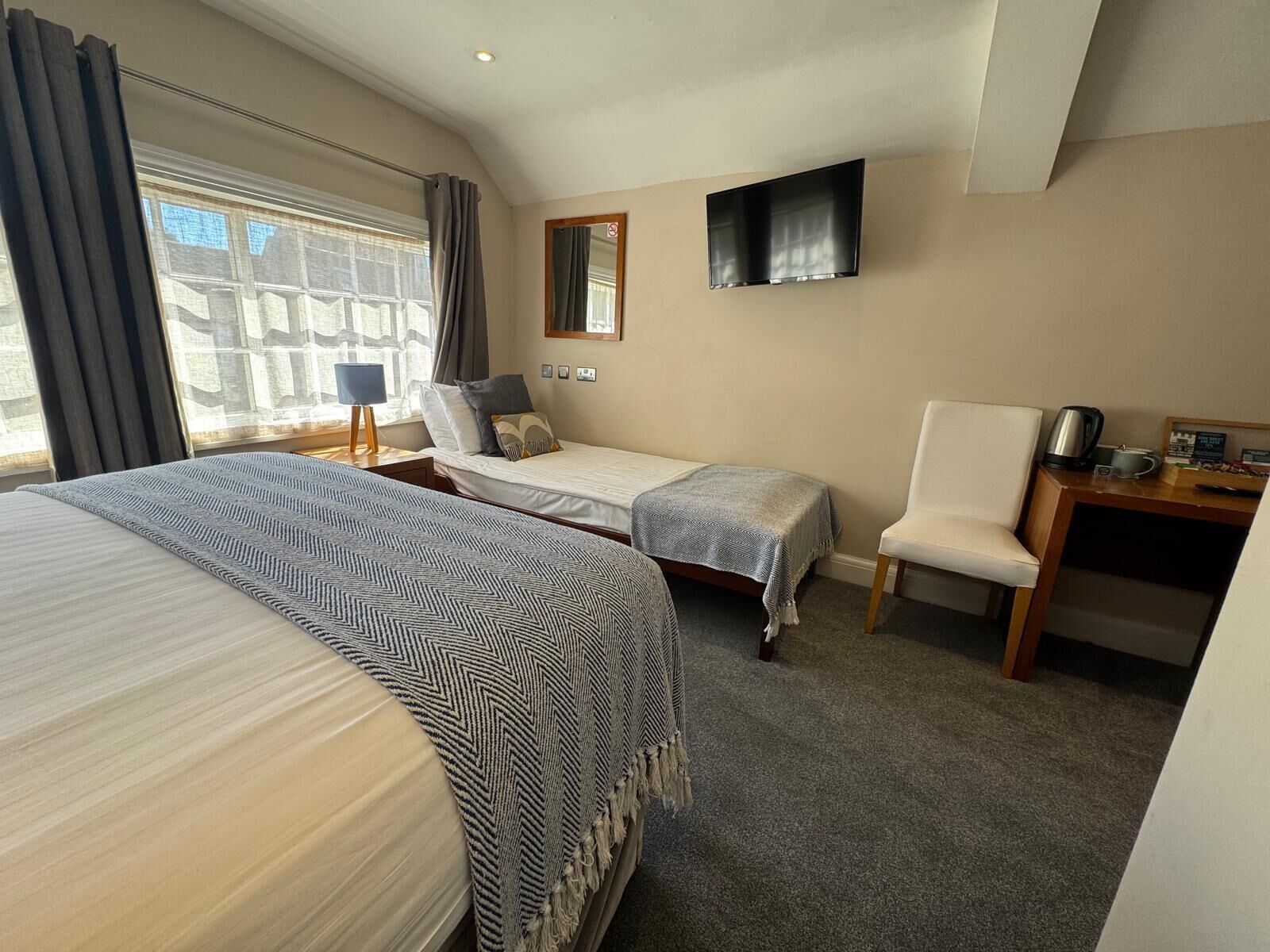 A hotel room with two beds, a desk, a chair, a TV, and a window with curtains.
