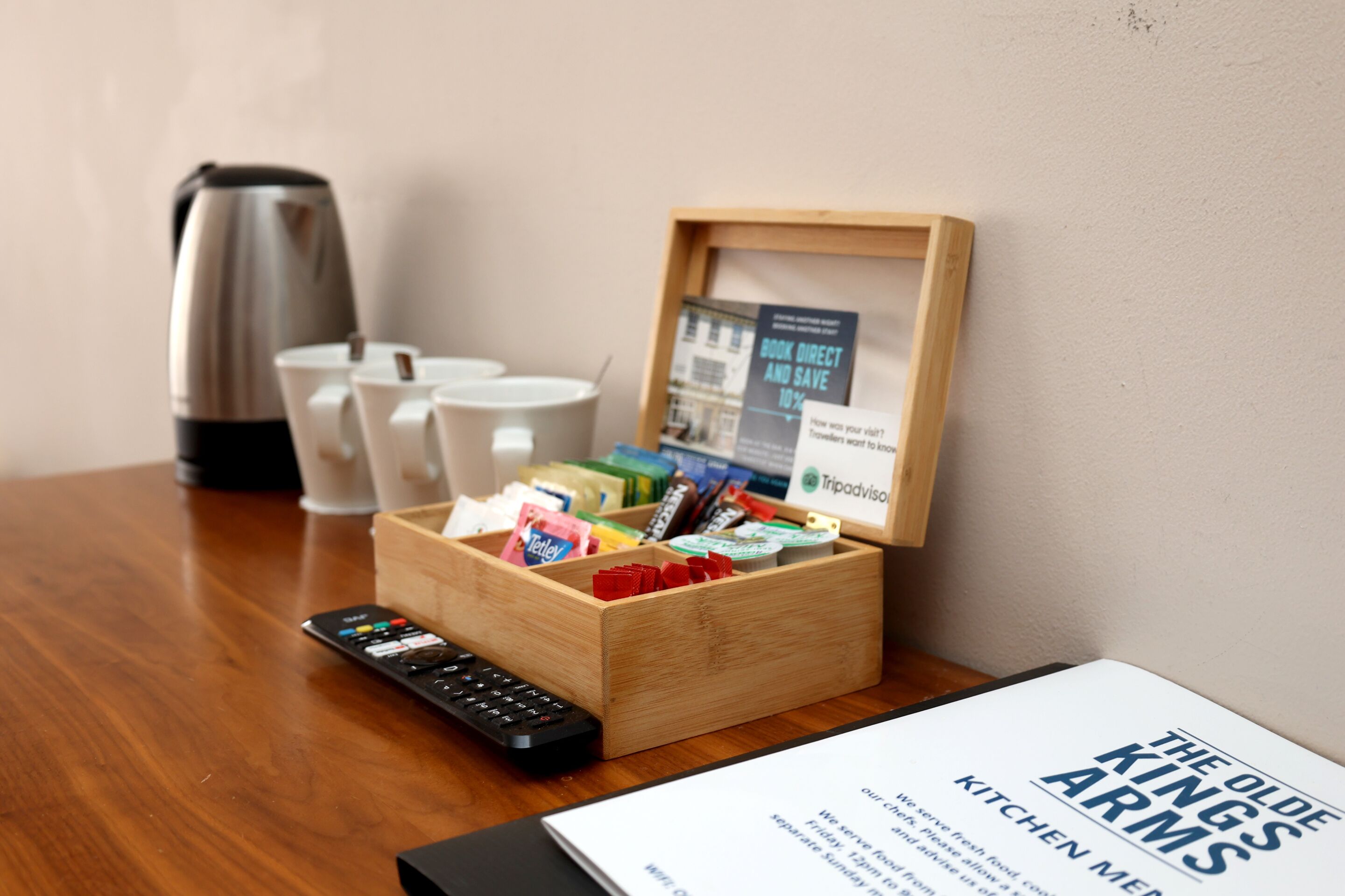 A wooden box with snacks and a TripAdvisor sign, a remote control, and a framed menu on a wooden table.