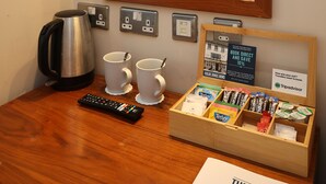 A hotel room with a wooden desk, a coffee maker, two mugs, a remote control, a tray of snacks, and a mirror with a wooden frame. - The Olde Kings Arms (Hemel Hempstead)