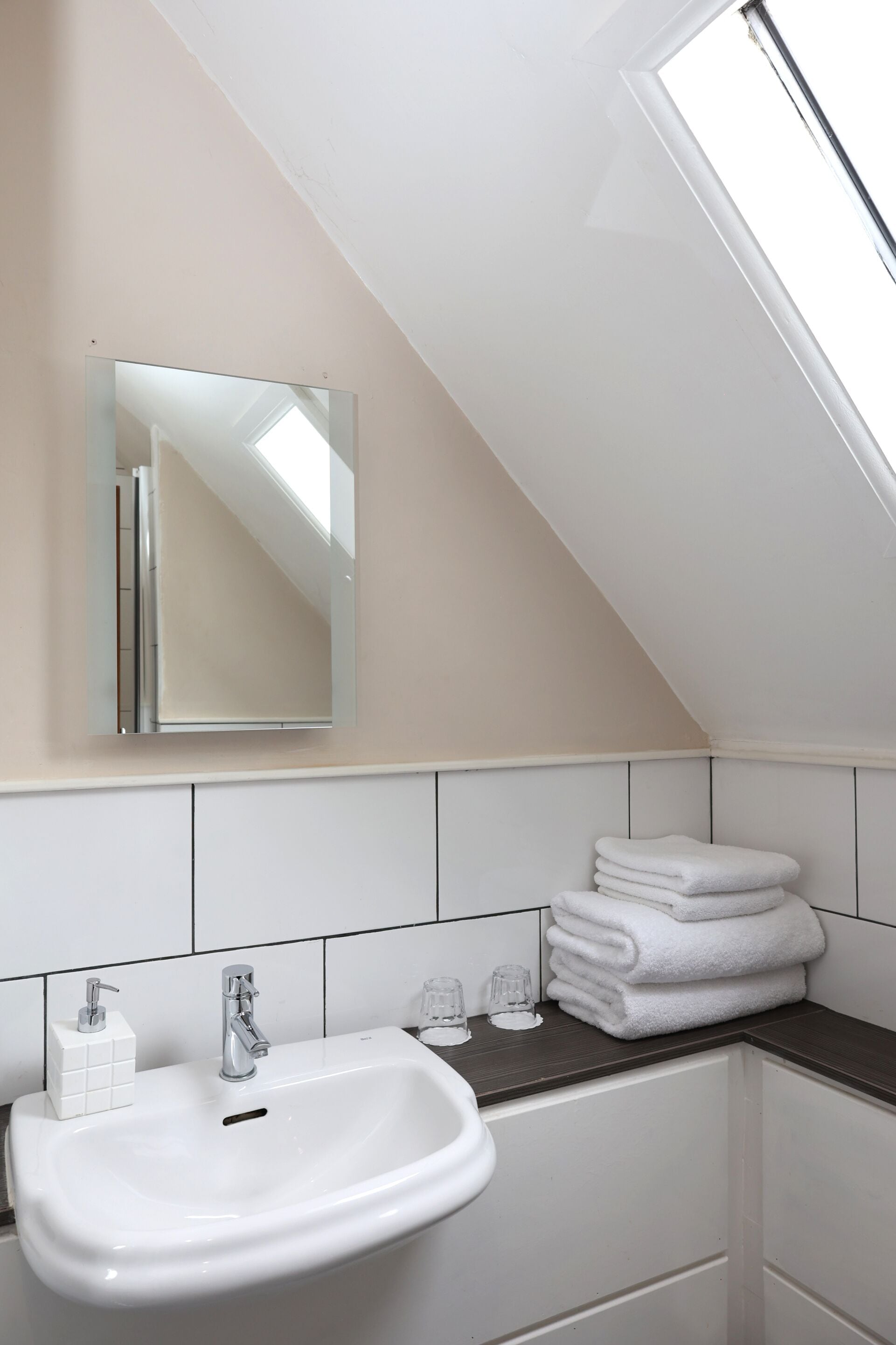 Een badkamer met een witte wastafel, spiegel en opgestapelde handdoeken.