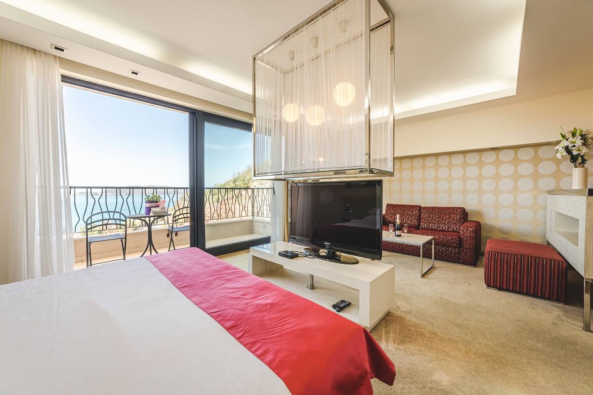 Una habitación de hotel moderna con una cama grande, un televisor de pantalla plana, un sofá y un balcón con mesa y sillas.
