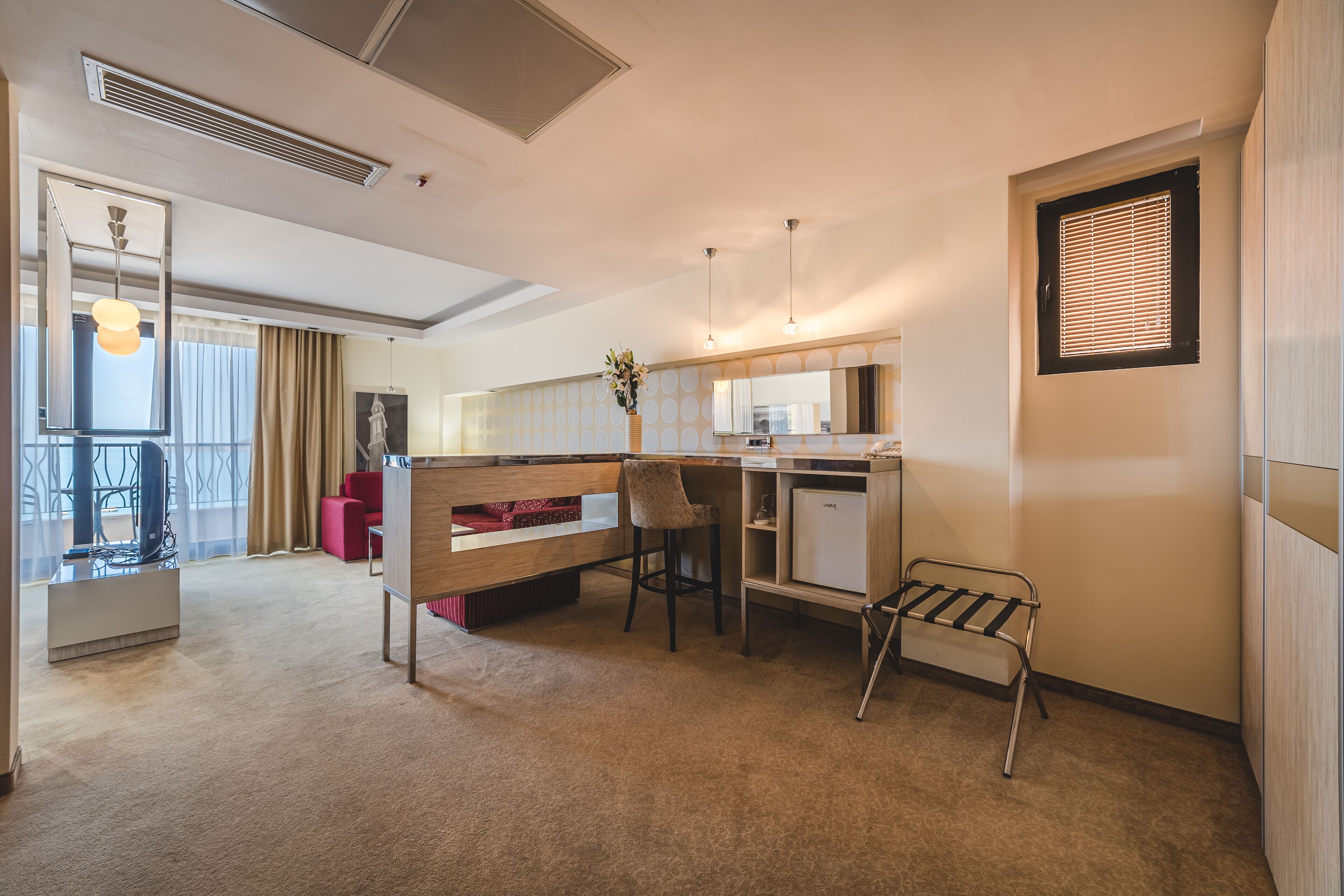 A modern hotel room with a bed, desk, chair, and a small seating area.
