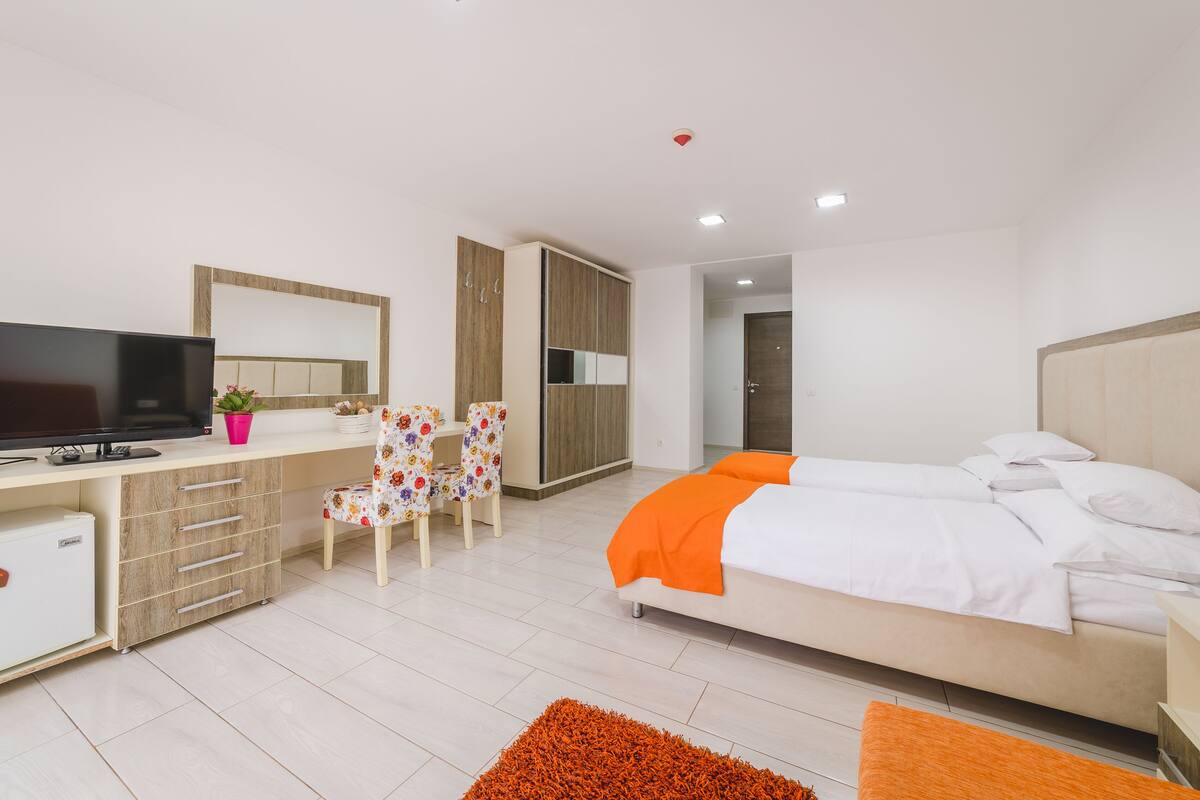 Un dormitorio moderno con una cama, un escritorio con computadora, una silla y un televisor.