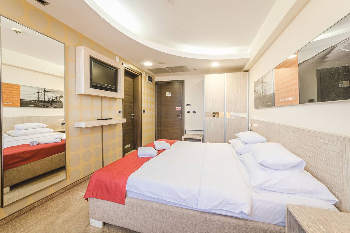 Habitación de hotel con cama, televisor montado en la pared, espejo y armario.