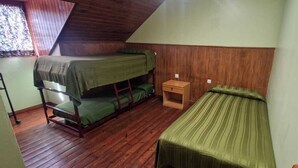 Une chambre de dortoir avec deux lits superposés, une petite table de chevet en bois et une fenêtre ornée d’un rideau à motifs floraux.