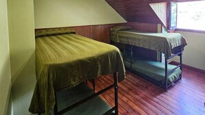 Une chambre de dortoir avec deux lits superposés, un plancher en bois et un plafond en pente doté d’un puits de lumière.