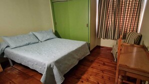 Une pièce avec un lit, une porte verte, une table en bois et une chaise.