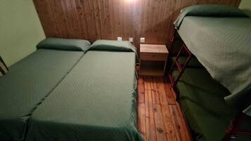 Una habitación pequeña y acogedora con dos camas individuales, una pared de madera y una pequeña mesa de madera.