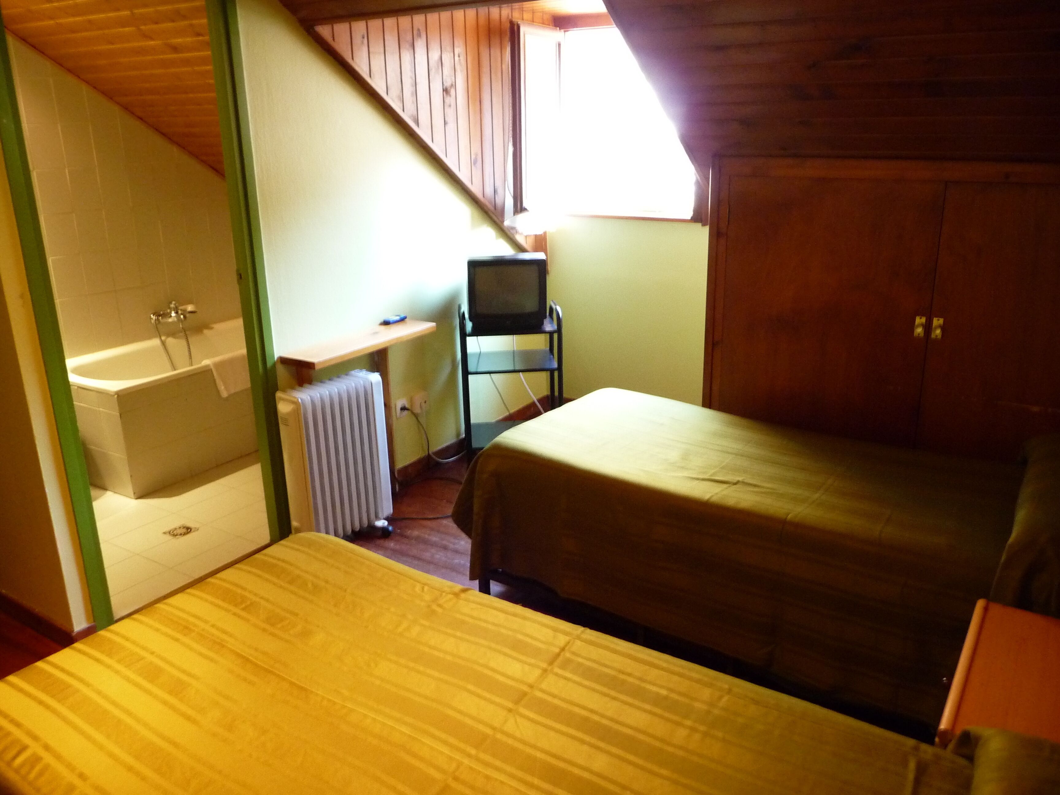 Een slaapkamer met een bed, een klein bureau met stoel, een radiator en een raam.