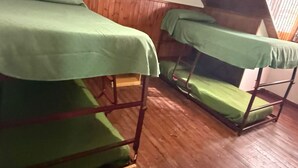 Des lits superposés recouverts de draps verts, dans une pièce aux murs et au sol en bois.