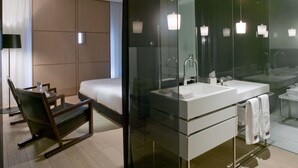 Une chambre d’hôtel moderne comprenant un lit, une coiffeuse en verre avec un lavabo, une chaise et un bureau.