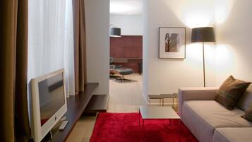 Una habitación de hotel moderna con una televisión de pantalla plana, una alfombra roja, un sofá, un escritorio y una silla.