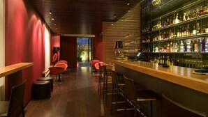 Un espace bar avec des chaises rouges, un comptoir en bois et des étagères remplies de bouteilles.
