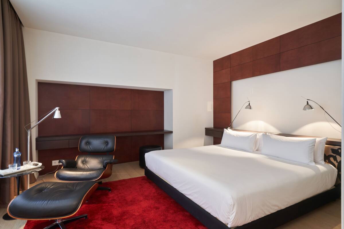 Ein Hotelzimmer mit einem großen Bett, einem Schreibtisch mit Stuhl, einem roten Teppich und einem braunen Kopfteil.