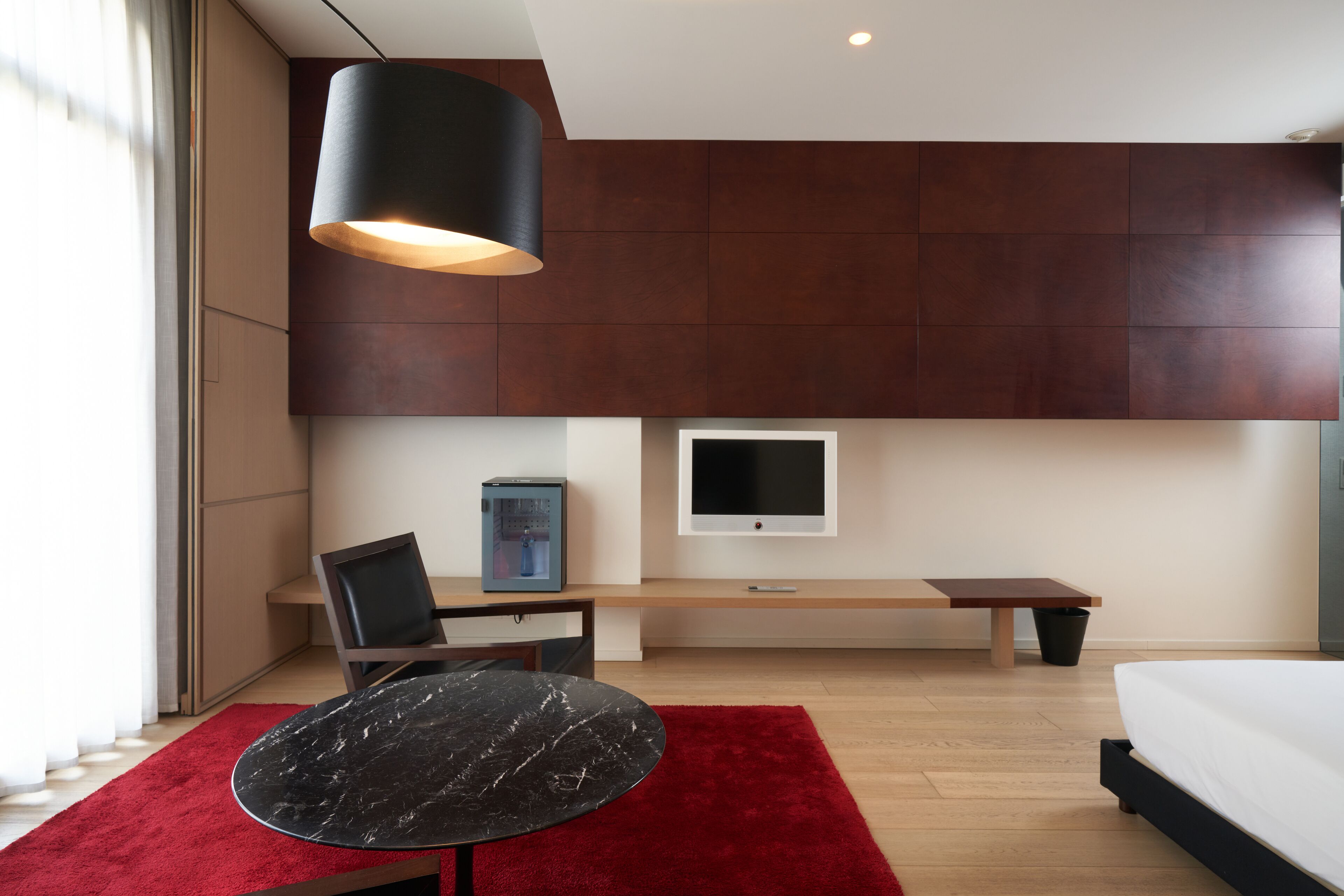 A modern bedroom with a bed, a desk, a chair, a TV, and a red rug.